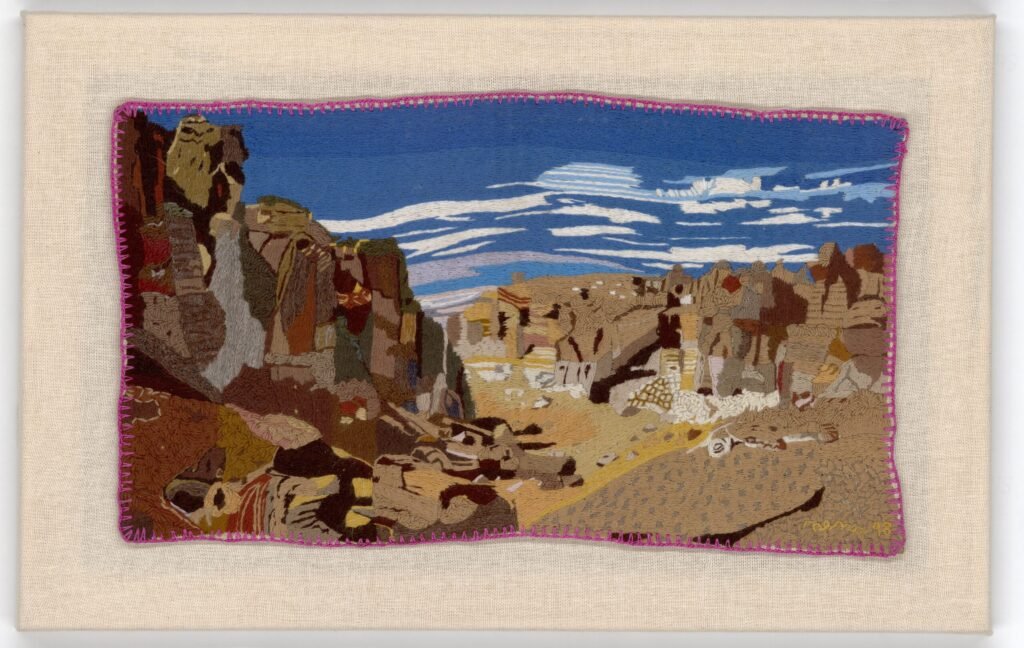 Registro digital de una obra de arpillera, se aprecia un paisaje desértico y rocoso con formaciones rocosas de diversos colores terrosos.
